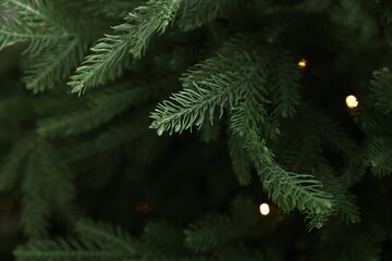 Branches of artificial Christmas tree against bokeh lights, closeup