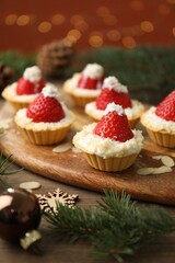 Christmas food. Tasty tartlets with strawberries, whipped cream, coconut flakes and decor on wooden table against background with blurred lights, closeup. Bokeh effect