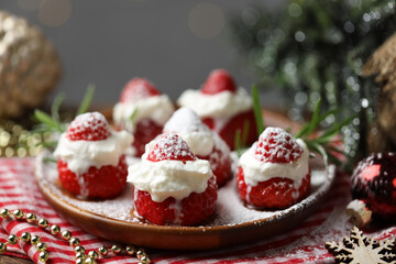 Christmas food. Santa hats made of strawberries, whipped cream, rosemary and decor on table against background with blurred lights, closeup. Bokeh effect
