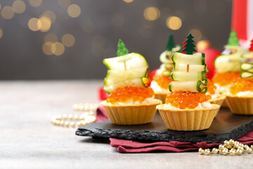 Tasty tartlets on grey textured table against blurred lights, closeup with space for text. Christmas appetizer