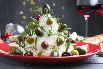 Delicious Christmas tree cheese ball with olives and rosemary on wooden table against grey background with blurred lights, closeup. New Year's appetizer