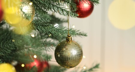 Christmas baubles and festive lights hanging on fir tree branches against blurred grey background, closeup with space for text. Bokeh effect