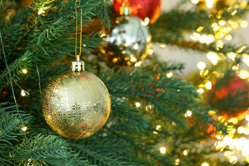 Christmas bauble hanging on fir tree branch against blurred lights, closeup with space for text. Bokeh effect