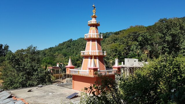 Hindu temple with a tall orange tower on a sunny day set against trees and clear blue sky