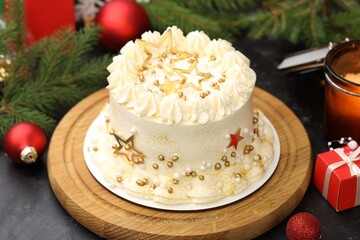 Delicious cake with Christmas decor and burning candle on black table, closeup