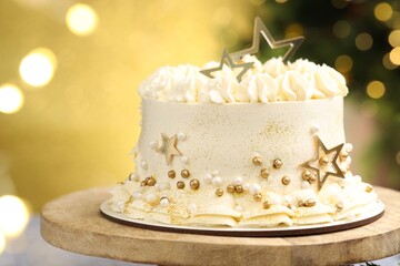Delicious cake with Christmas decor on stand against golden background with blurred lights, closeup