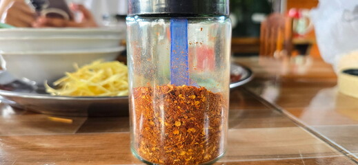 Chili powder is packaged in a clear bottle with a black cap and placed on the dining table. Crushed red pepper is a spicy seasoning. Dried chilies are finely ground to be used spicy seasoning in food.