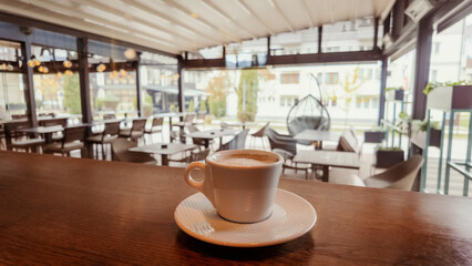 Cup of coffee on wooden counter inside modern cafe with bright interior, natural light and cozy atmosphere, perfect for lifestyle or hospitality concepts