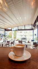 Vertical shot of coffee cup on wooden table inside bright modern cafe, relaxing atmosphere ideal for hospitality, design, and lifestyle themes