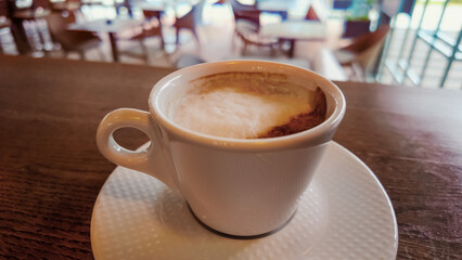Close-up of hot coffee cup with foam on wooden counter, blurred cafe background emphasizing warmth, aroma, and relaxation