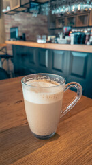Glass cup of frothy coffee on wooden table inside stylish cafe bar, cozy interior design perfect for branding and lifestyle visuals