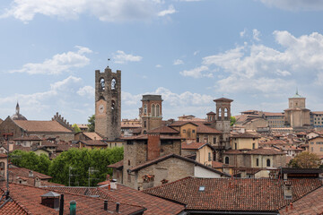 Panoramic view of upper town in Bergamo with tall Civic Tower rising among red tiled roofs, church domes, and bell towers that shape timeless skyline of Lombard heritage