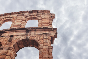Obraz premium Minimal view of Verona Arena shows upper arches of Roman amphitheater rising against dense gray clouds, emphasizing its monumental form