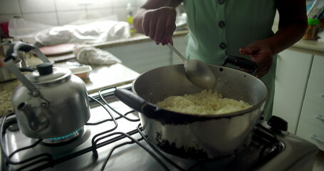 Close-up of a woman stirring rice in a pot on a stovetop, capturing the essence of home cooking, warmth, and tradition in an intimate kitchen setting
