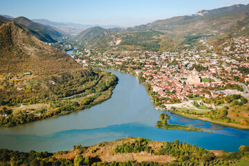 Aerial view of Mtskheta, Georgia, with confluence of rivers Aragvi and Kura, traditional red-roof houses and Svetitskhoveli Cathedral on a clear autumn day. Tranquil and scenic landscape © Anna
