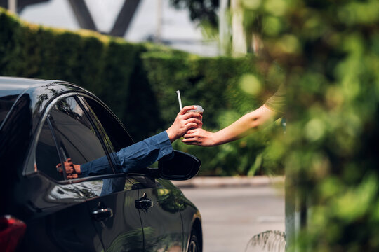 Hand Man in car receiving coffee in drive thru fast food restaurant. Staff serving takeaway order for driver in delivery window. Drive through and takeaway for buy fast food for protect covid19.