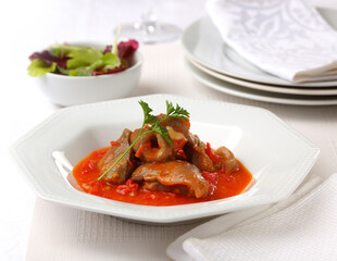 Pork with tomato sauce and garnished with parsley, served on a white plate.