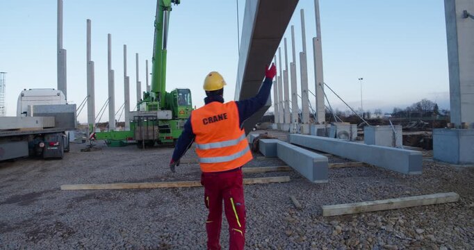 Supervised construction crew coordinates crane-assisted transport and installation of a precast structural column for industrial frame assembly. Safety vests, helmets, and teamwork highlighted.
