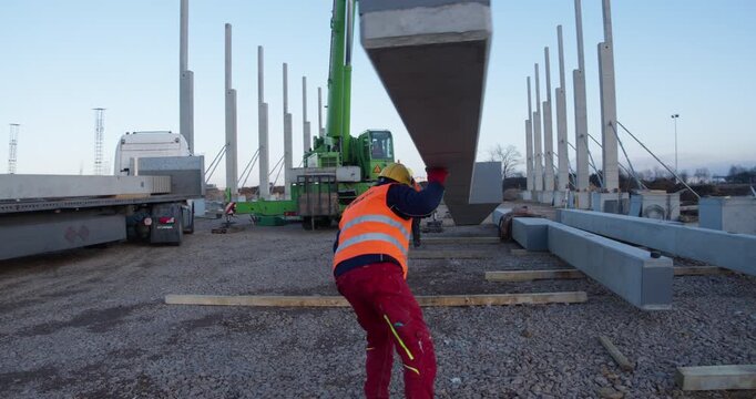 Supervised construction crew coordinates crane-assisted transport and installation of a precast structural column for industrial frame assembly. Safety vests, helmets, and teamwork highlighted.