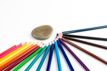Colorful Pencil Set Arranged in Rainbow Arc With Smooth Stone on White Background