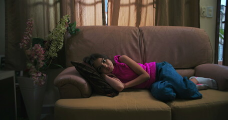 Young girl lying on a couch with a distant gaze, expressing solitude, sadness, and childhood...