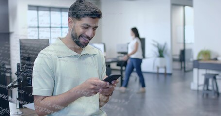 Standing Asian Indian office worker holding smartphone by row of desks in modern open-plan office