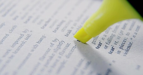 Highlighting printed word tear on dictionary page with neon yellow highlighter pen, copy space
