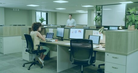 Working woman focusing on laptop and monitor charts at open office desk, colleague pointing