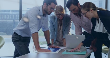 Collaborating colleagues leaning around meeting table in office with laptop and printed charts