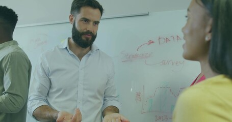 Gesturing man with beard talking in boardroom, with whiteboard showing data charts arrows graph