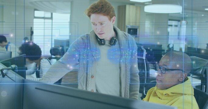 Standing software engineer in cardigan and headphones next to developer in office, with monitors