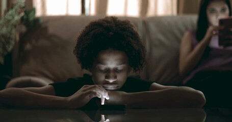 Boy leaning on table staring at smartphone, illuminated by screen light, distant expression, emotional isolation and apathy in digital age captured