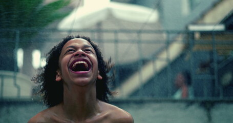 Smiling child of African descent under water spray, face lifted in pure joy, arms stretched wide,...