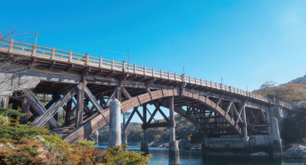 A weathered wooden bridge spans a waterway under a clear, bright blue sky