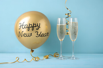 Gold “Happy New Year” balloon with champagne flutes and ribbon on blue—festive, refined setup evoking joy, elegance, and celebration for the new year. generative ai