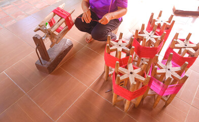 Traditional hand reel yarn preparation with red silk thread on wooden spools, showing local craftsmanship and textile culture in rural Thailand