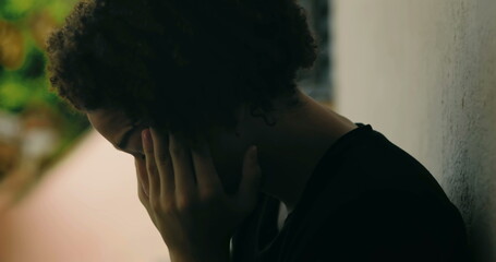 Young boy in emotional breakdown, hands covering face, standing against wall, African descent,...