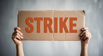 A person holds up a cardboard sign with the word STRIKE written in large orange letters.