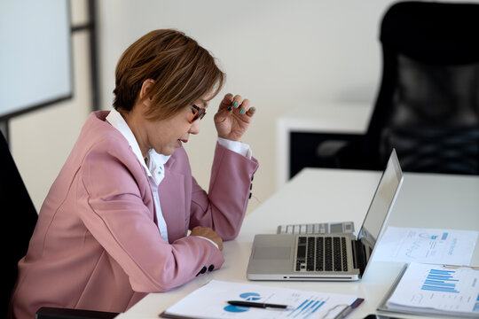 Asian adult business professional woman analyzes market data using laptop computer for strategic planning and executive decision making in modern office - Powered by Adobe