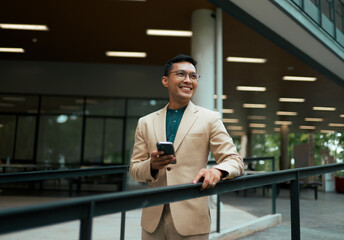 Smiling Asian businessman holding phone standing in modern building