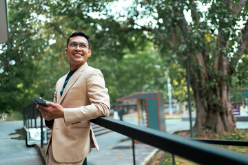 Smiling businessman holding smartphone outdoors contemplating future © PaeGAG