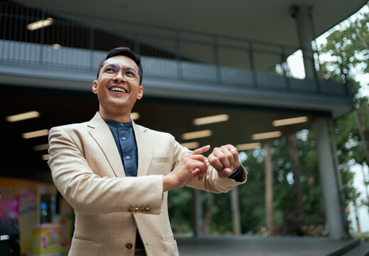 Happy Asian businessman checking smart watch smiling outdoors