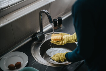 Close-up of hands washing dishes in kitchen sink under running water