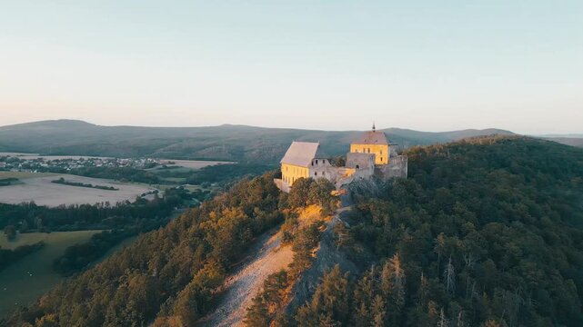 Nestled on a hilltop, Tocnik Castle stands majestically as the sun sets, casting warm hues across the ancient structure and surrounding landscape.