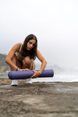 Young woman rolling yoga mat by the sea