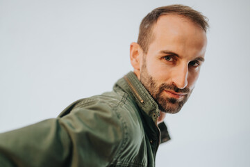 Close-up captured image of a man with a confident demeanor, wearing a green jacket, looking...