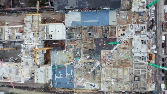 Direct overhead drone shot of large-scale residential building construction site with visible cranes, frameworks, and workers. Urban housing and industry progress.