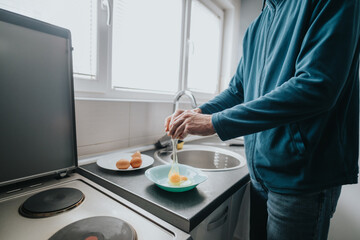 A person cracks an egg into a bowl on a modern kitchen counter, preparing ingredients.