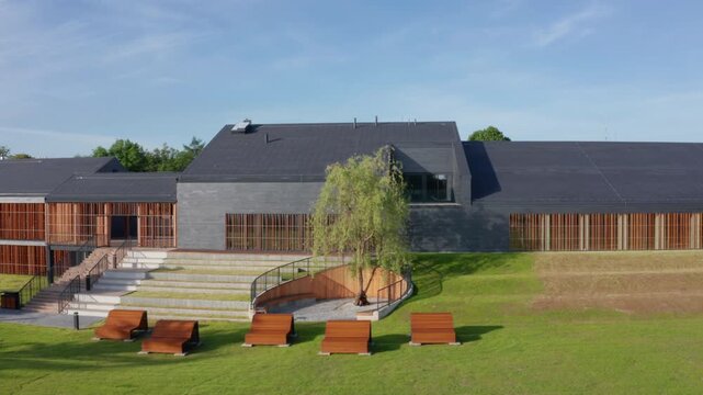 Aerial lateral movement along modern slate and timber-clad public pool, Eisenberga Street Krakow, with sun lounges in landscaped park setting.