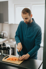 A focused individual preparing a healthy meal by slicing carrots in a well-lit kitchen.